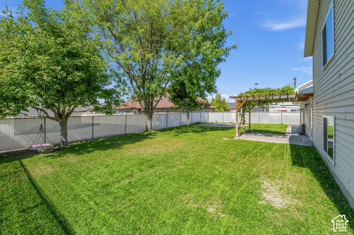 Expansive backyard with a manicured lawn, established trees, and a shaded patio featuring a wooden pergola
