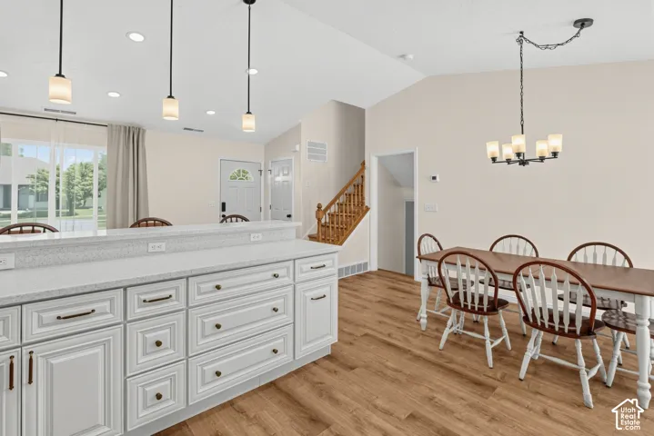 Open-concept room featuring wood-finish flooring, white cabinetry with dark hardware, a light-toned countertop, and recessed ceiling lighting