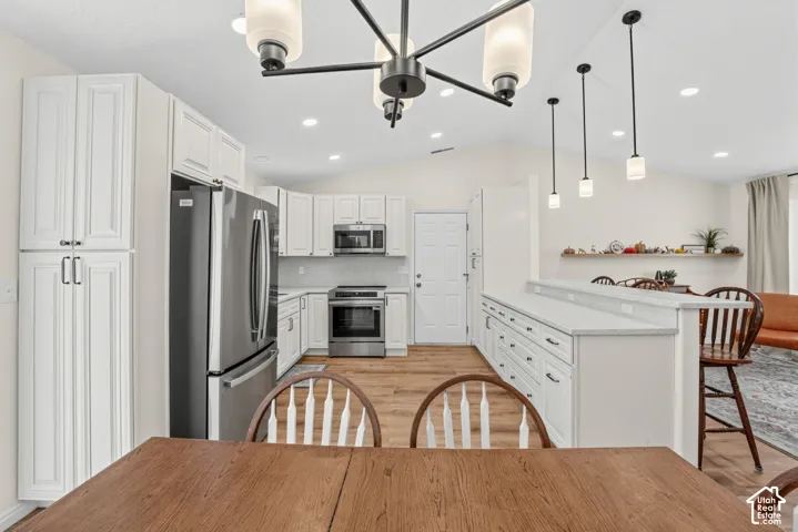 Kitchen featuring white cabinetry, stainless steel appliances, wood-finish flooring, a breakfast bar, and vaulted ceilings