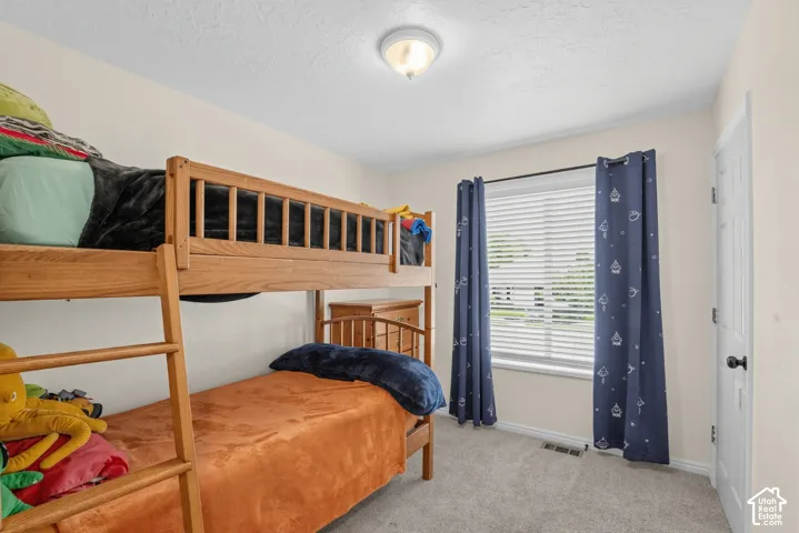 Neutral wall paint, ceiling-mounted light fixture, window with blinds, carpeted flooring, and a white door with black hardware