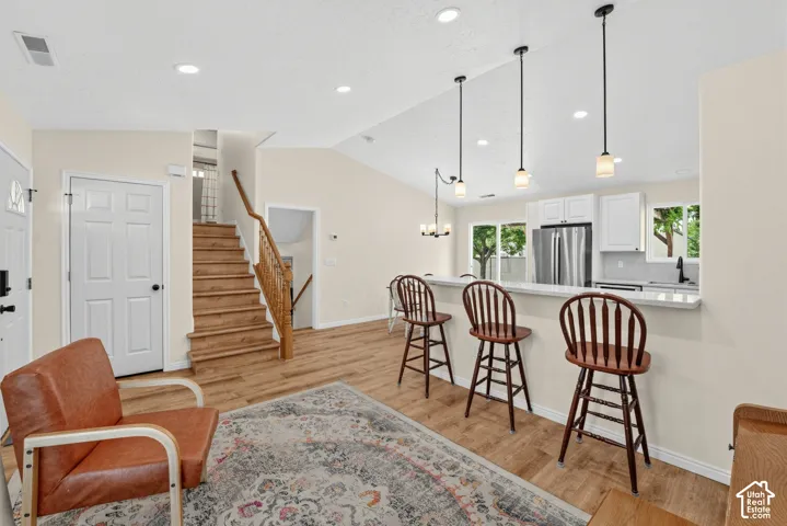 Wood-finish flooring throughout, vaulted ceiling, recessed lighting, and kitchen with white cabinetry and stainless steel appliances