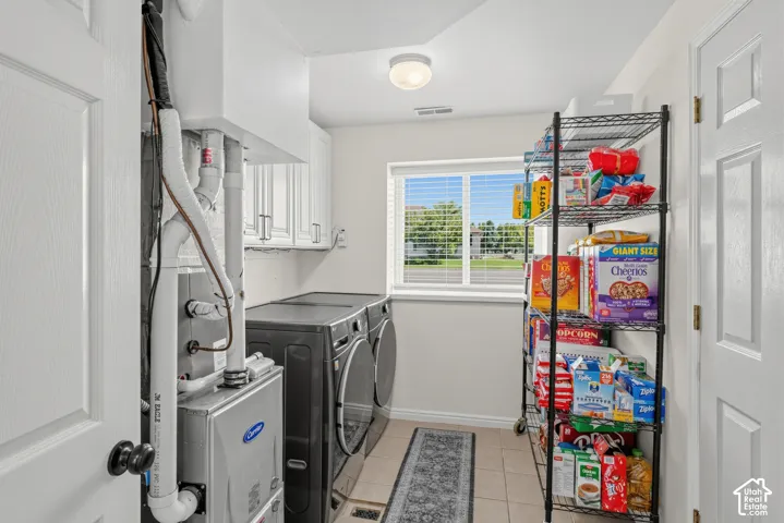Utility room featuring tile flooring, white upper cabinetry, and a window with blinds