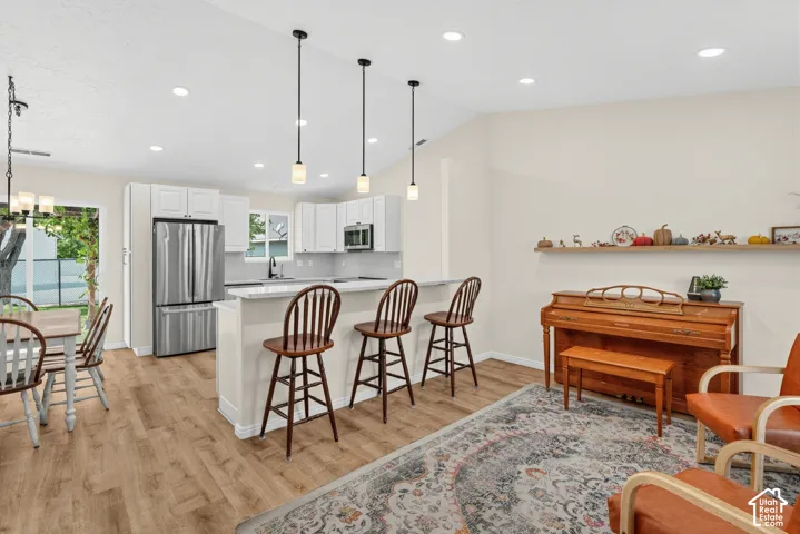 Open-concept living area featuring a kitchen island with seating, stainless steel appliances, wood-finish flooring, and pendant lighting