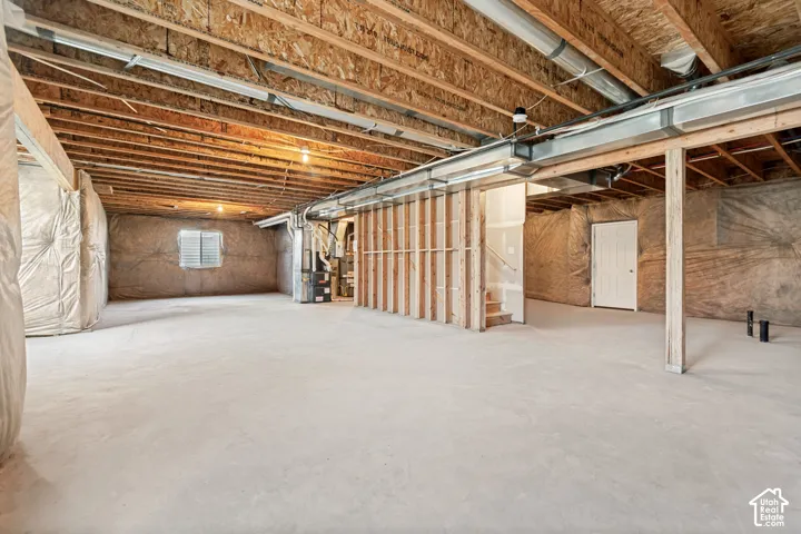 Unfinished basement featuring exposed wood joists, concrete flooring, a window, and framed walls