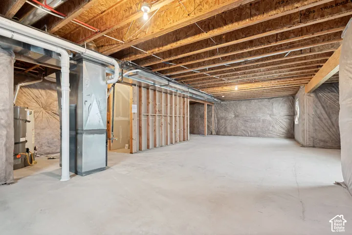 Unfinished basement featuring concrete flooring, exposed wood joists, utility piping, and partially framed walls