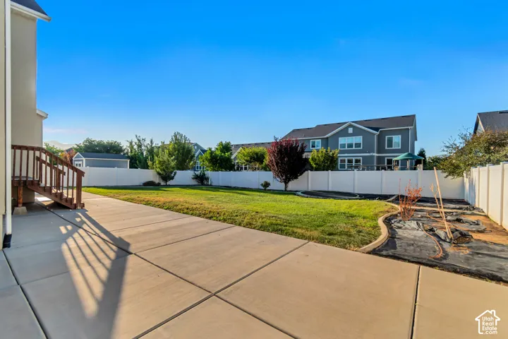 Expansive concrete patio with direct access to a grassy lawn, complemented by a white privacy fence