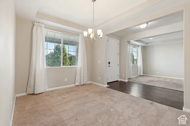 Carpeted interior space with a multi-pane window, suspended chandelier, and a white paneled door