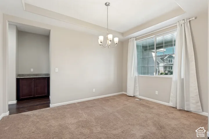Tray ceiling with a central chandelier, large window with natural light, built-in cabinetry with a stone countertop, and dark wood-finish flooring