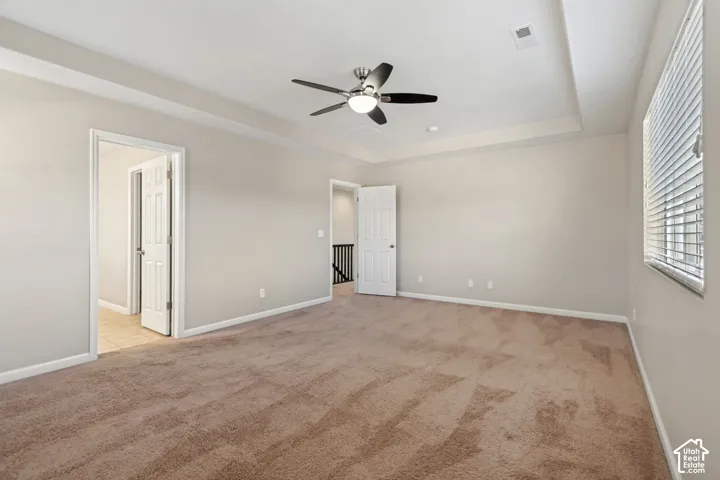 Tray ceiling with recessed lighting, ceiling fan with integrated lighting, window with blinds, and neutral tone carpet