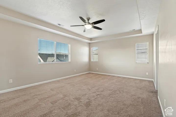Spacious room featuring neutral carpeting, a ceiling fan with integrated lighting, and multiple windows with horizontal blinds