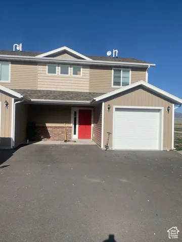 Two-story exterior with light brown siding, a red front door, an attached garage, and an asphalt driveway