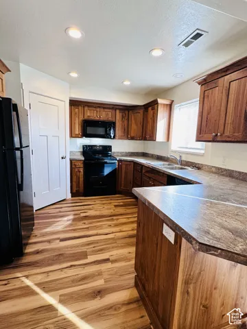 Kitchen featuring wood-finish flooring, recessed lighting, wood cabinetry, dark countertops, and a full suite of black appliances