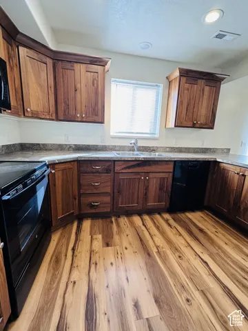 Wood-finish flooring, L-shaped countertop, recessed lighting, double basin sink, and black appliances