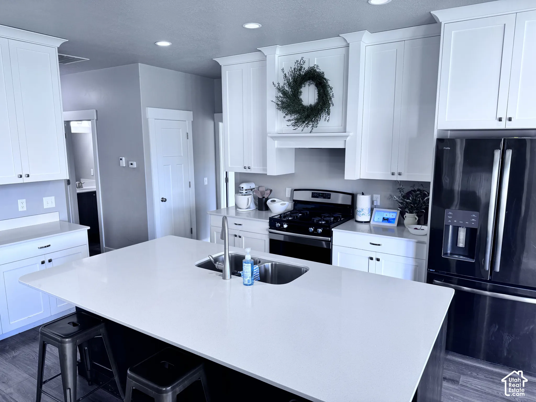 Kitchen featuring white cabinetry, a large center island with an undermount sink, stainless steel appliances, recessed lighting, and wood-finish flooring