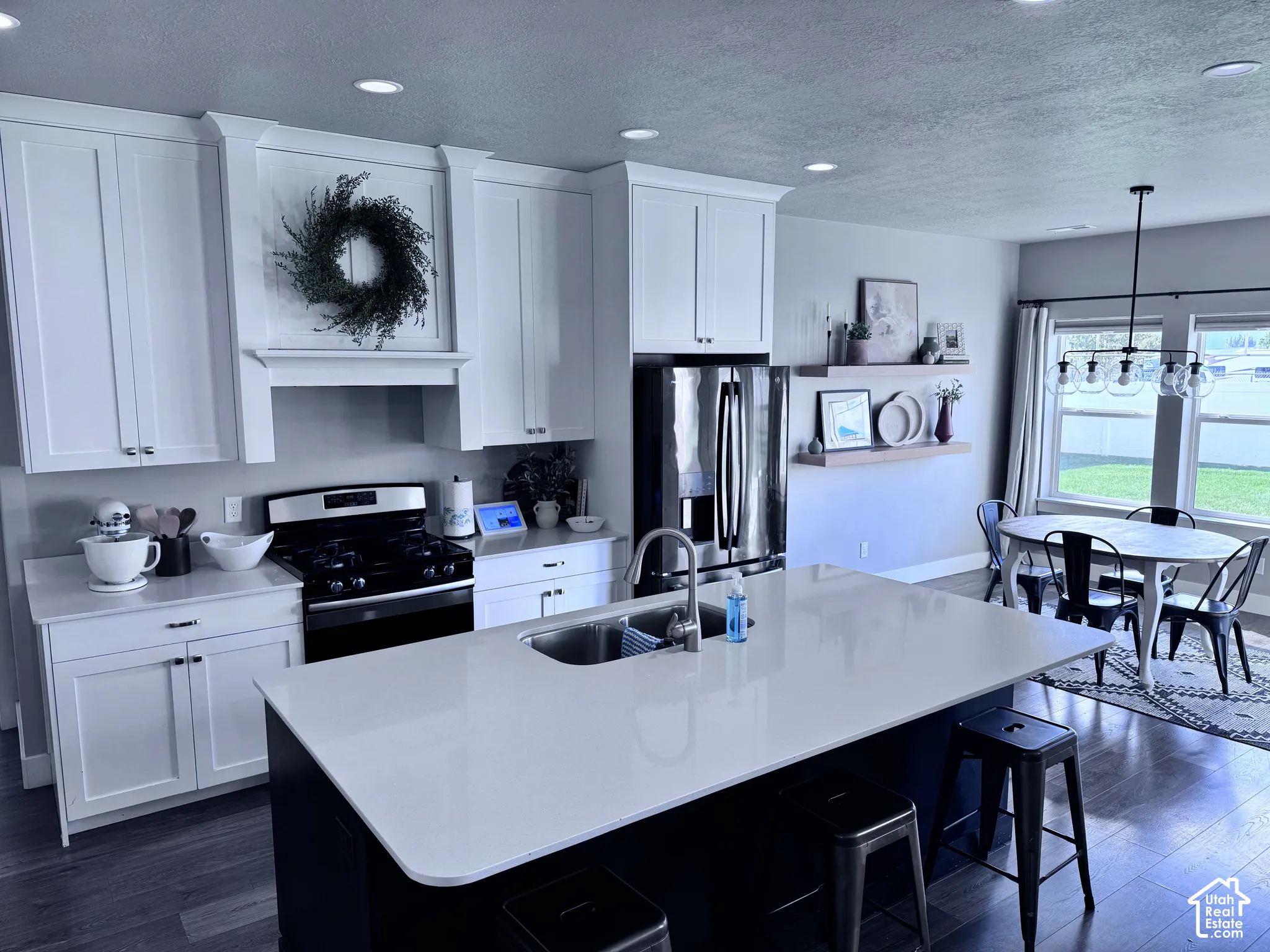 Kitchen featuring recessed lighting, white cabinetry, a large kitchen island with integrated sink, stainless steel appliances, and wood-finish flooring