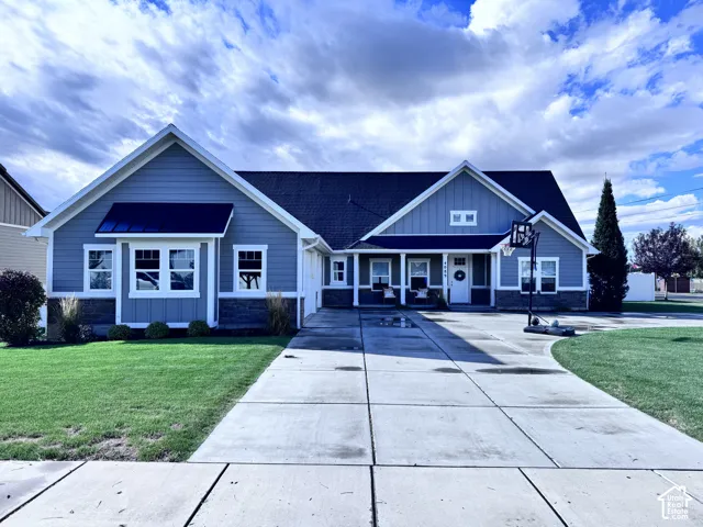 Blue siding exterior with white trim, dark shingle roof, stone accent foundation, front porch, and concrete driveway