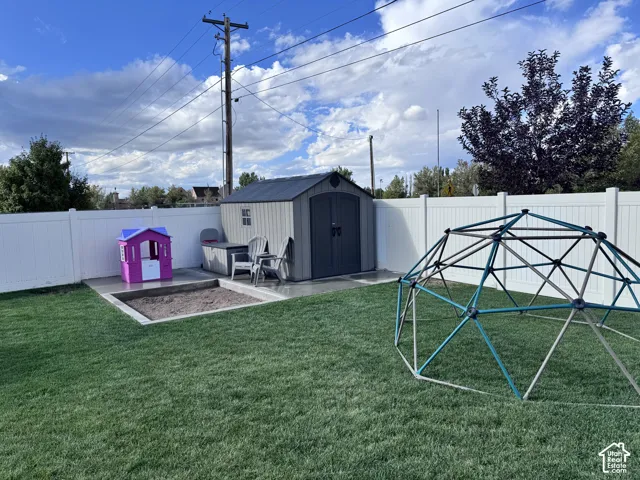 Fenced backyard featuring a gravel-filled sandbox, concrete patio, and storage shed