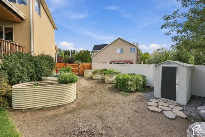 Fenced backyard space featuring multiple raised garden beds, a storage shed, and a stone paver path