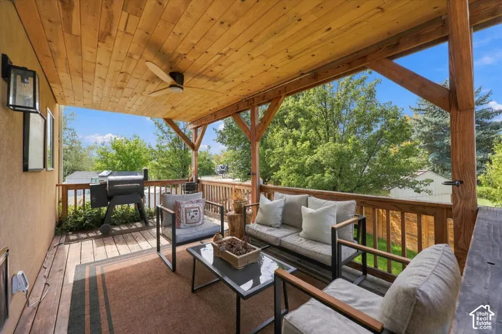Covered wood-plank deck with a ceiling fan, wood railing, and exterior wall sconces