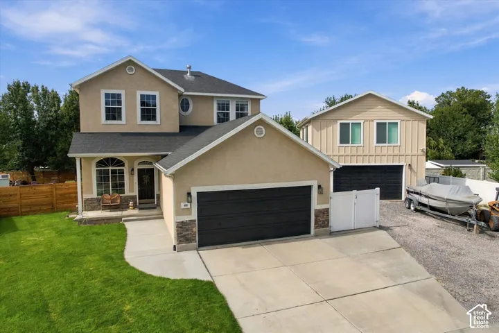 Stucco exterior with stone accents, attached two-car garage, separate two-story garage with additional bay, concrete driveway, and front lawn