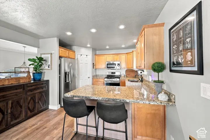 Kitchen featuring recessed lighting, stainless steel appliances, wood-finish flooring, light wood cabinetry, and a granite countertop island with seating