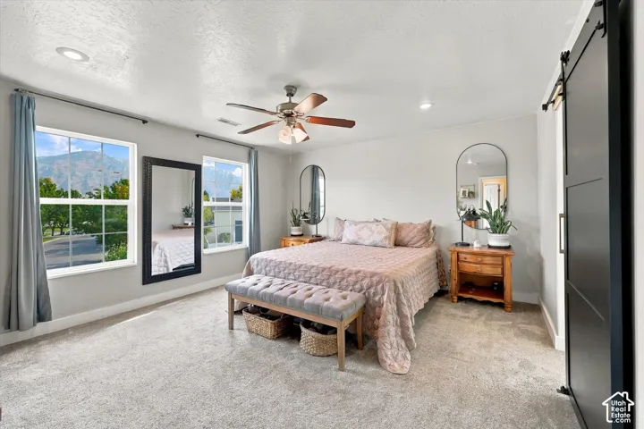 Recessed lighting, ceiling fan, carpeting, two large windows, and a black barn door