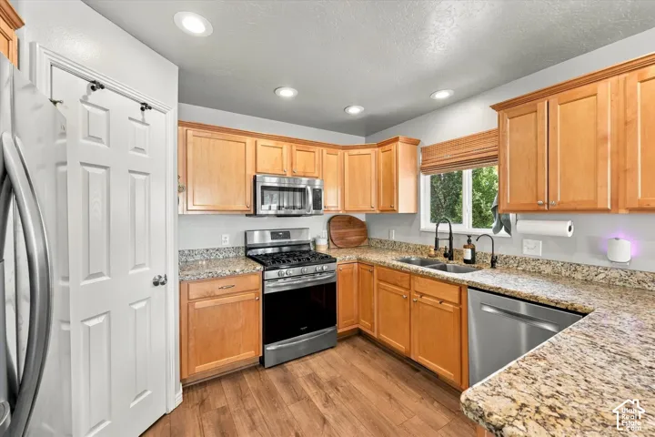 Kitchen featuring wood-finish flooring, light wood cabinetry, stainless steel appliances, granite-style countertops, and recessed lighting