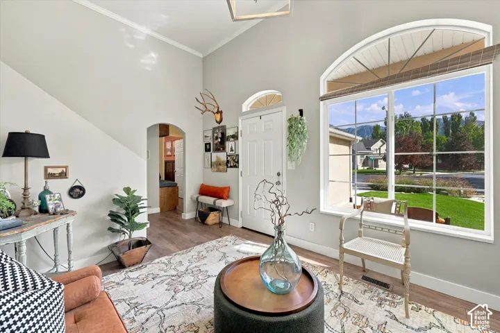 Vaulted ceilings with crown molding, wood-finish flooring, an arched entryway, and a large arched window with grid patterns