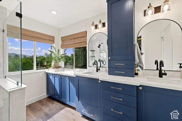 Dual vanity with deep blue cabinetry, white countertops, built-in storage, arched mirrors, and wood-finish flooring
