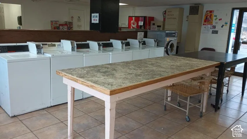 Tiled flooring extending throughout, multiple top-load washing machines, and a front-load washing machine