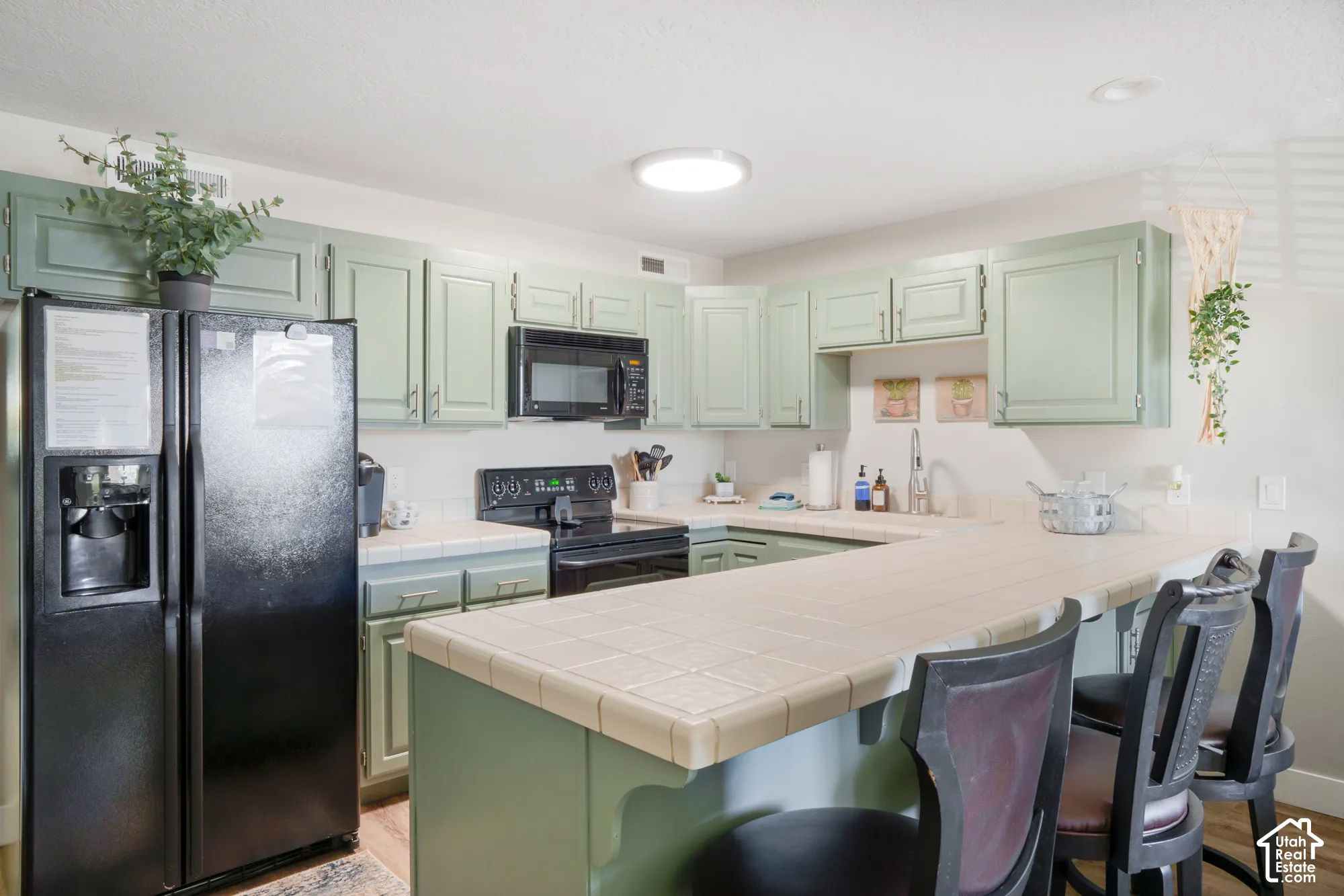 U-shaped kitchen featuring light green cabinetry, tile countertops, and a black appliance suite including a refrigerator, oven, and microwave
