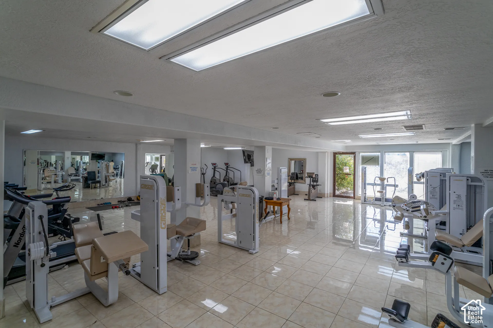 Expansive fitness center featuring tiled flooring, recessed lighting, and large mirrored walls in main clubhouse lower level