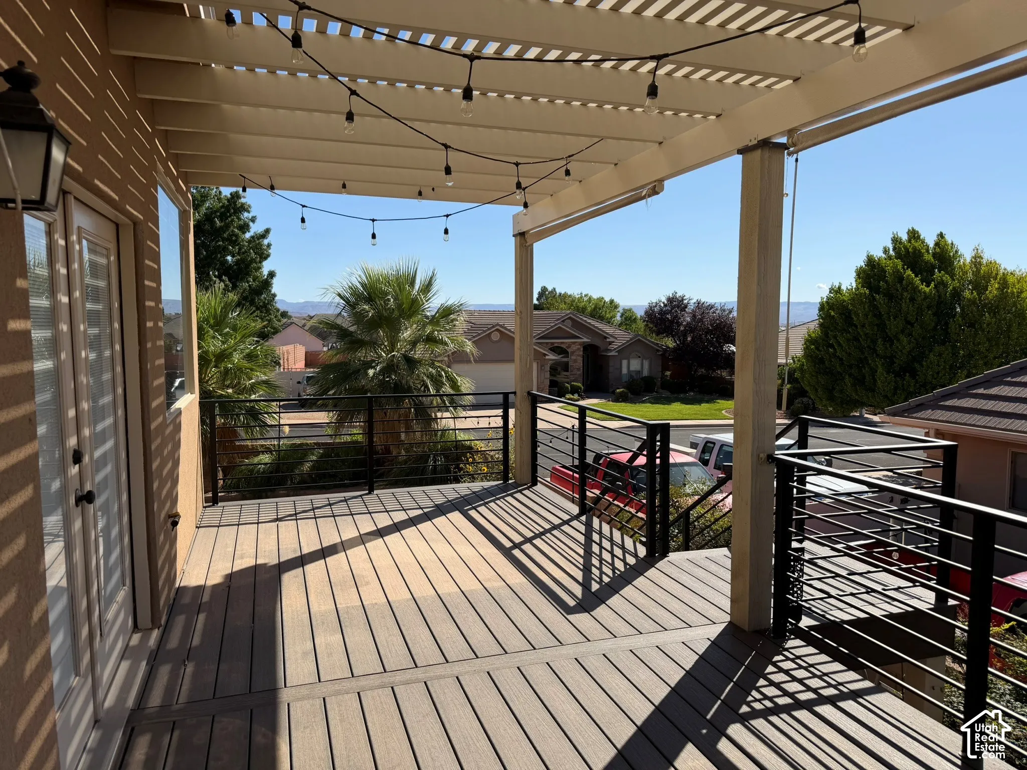 Covered wood-finish deck with a pergola-style ceiling, black metal railings, and attached exterior lighting