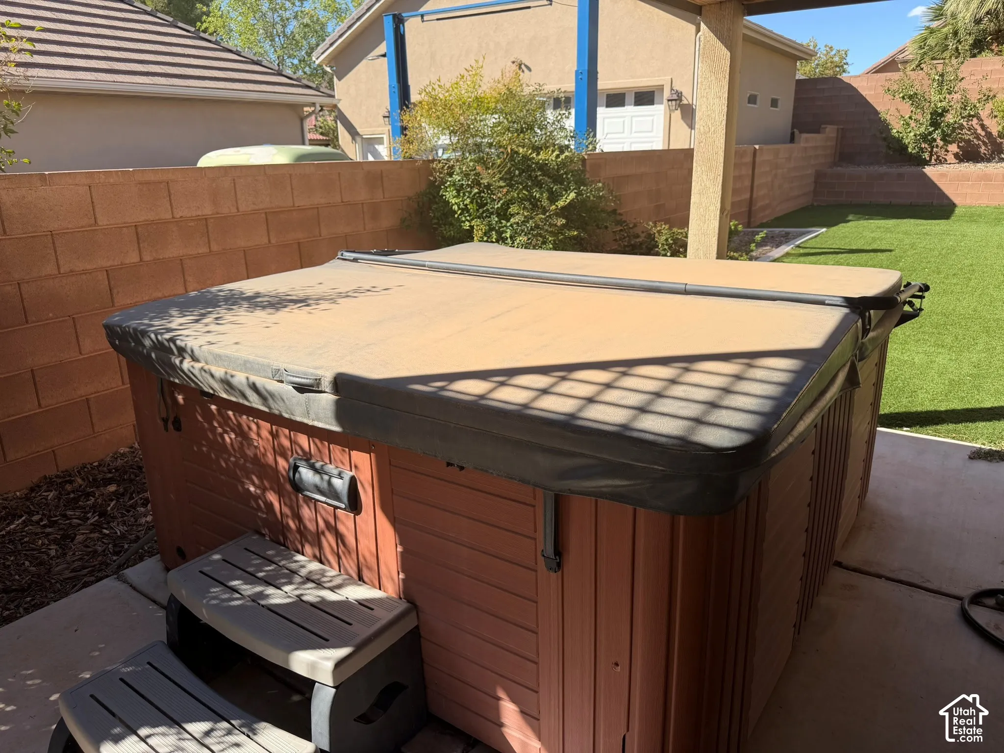 Spa with a protective cover, integrated steps, and wood-finish paneling, situated on a concrete patio