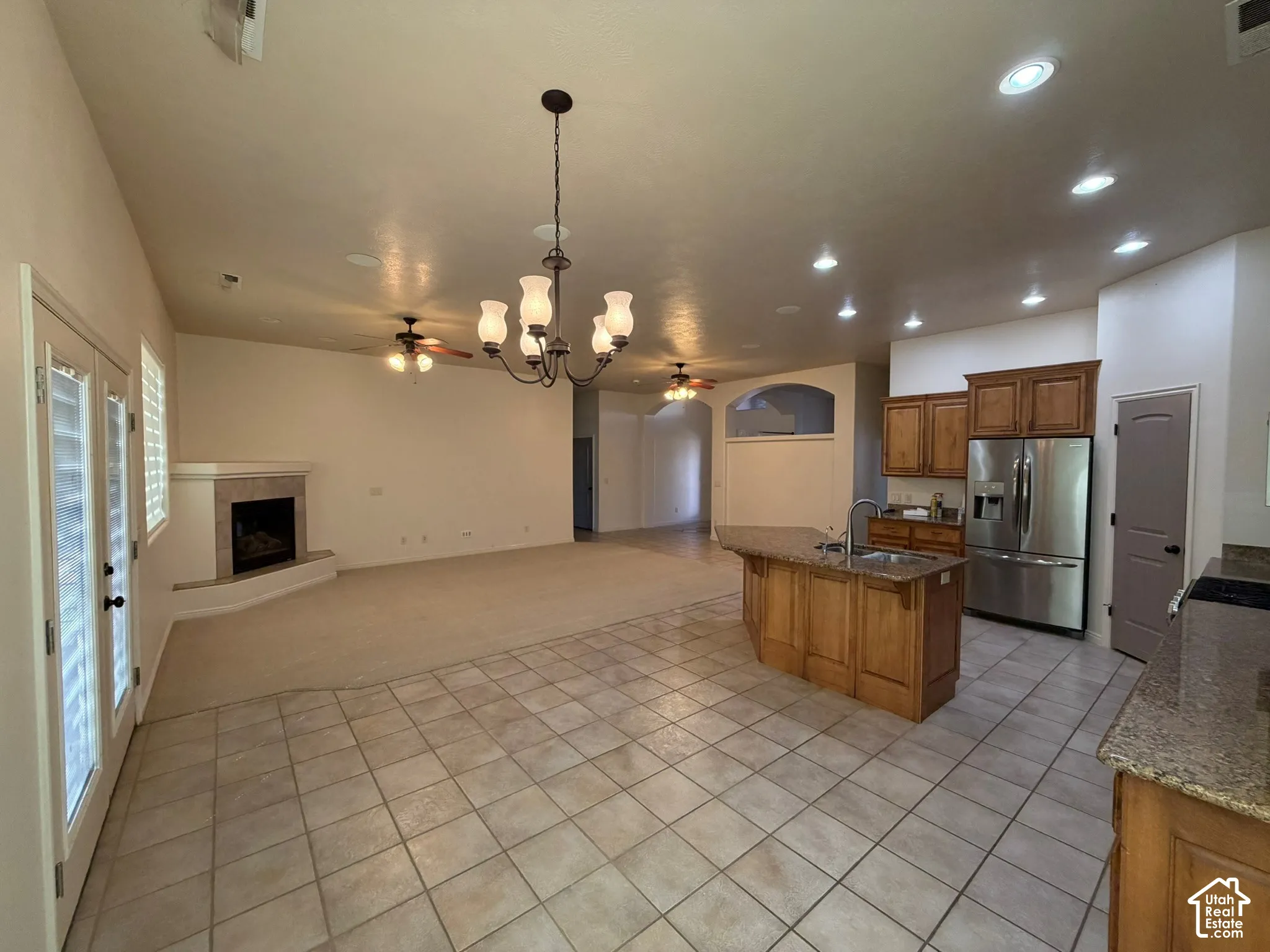 Open-concept kitchen and living area featuring a central island with sink, wood cabinetry, stainless steel appliances, and a fireplace with a tile surround