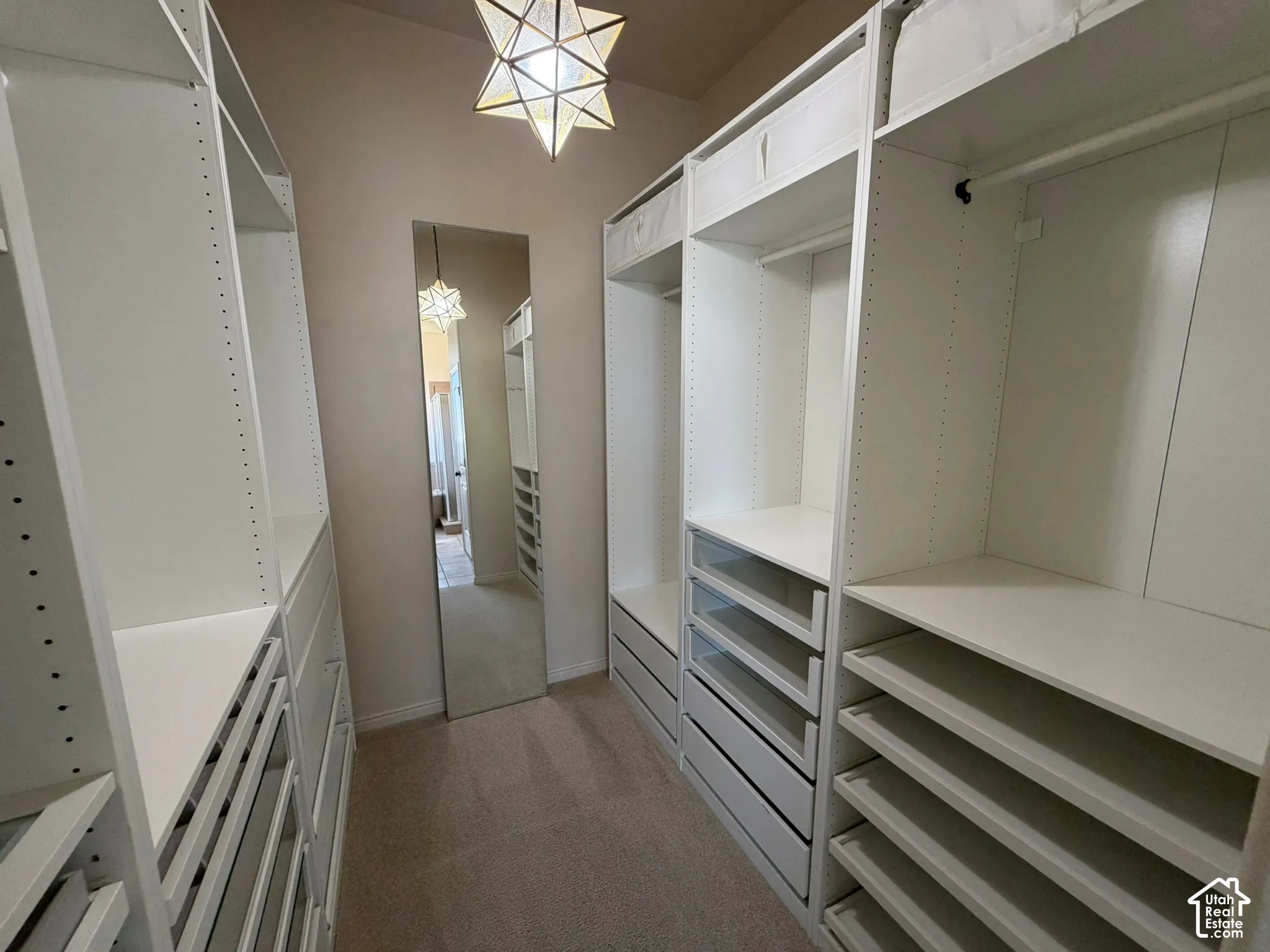 Walk-in closet with extensive white built-in shelving, multiple hanging rods, integrated drawers, and a full-length mirror