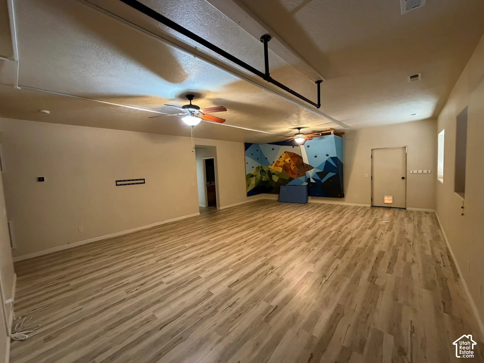 Spacious room featuring wood-finish flooring, two ceiling fans, and a climbing wall