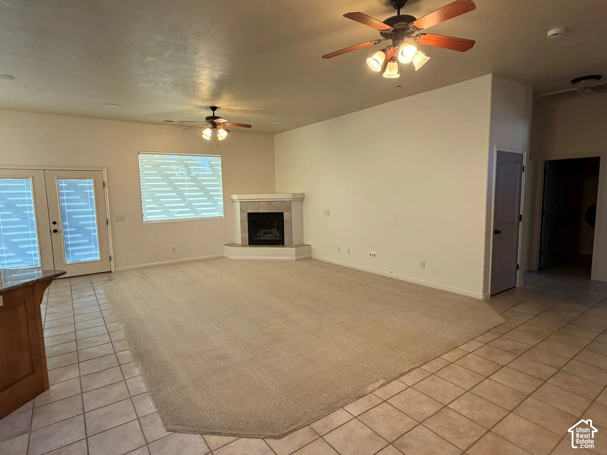 Spacious living area featuring a corner fireplace, multiple ceiling fans, and a combination of carpet and tile flooring