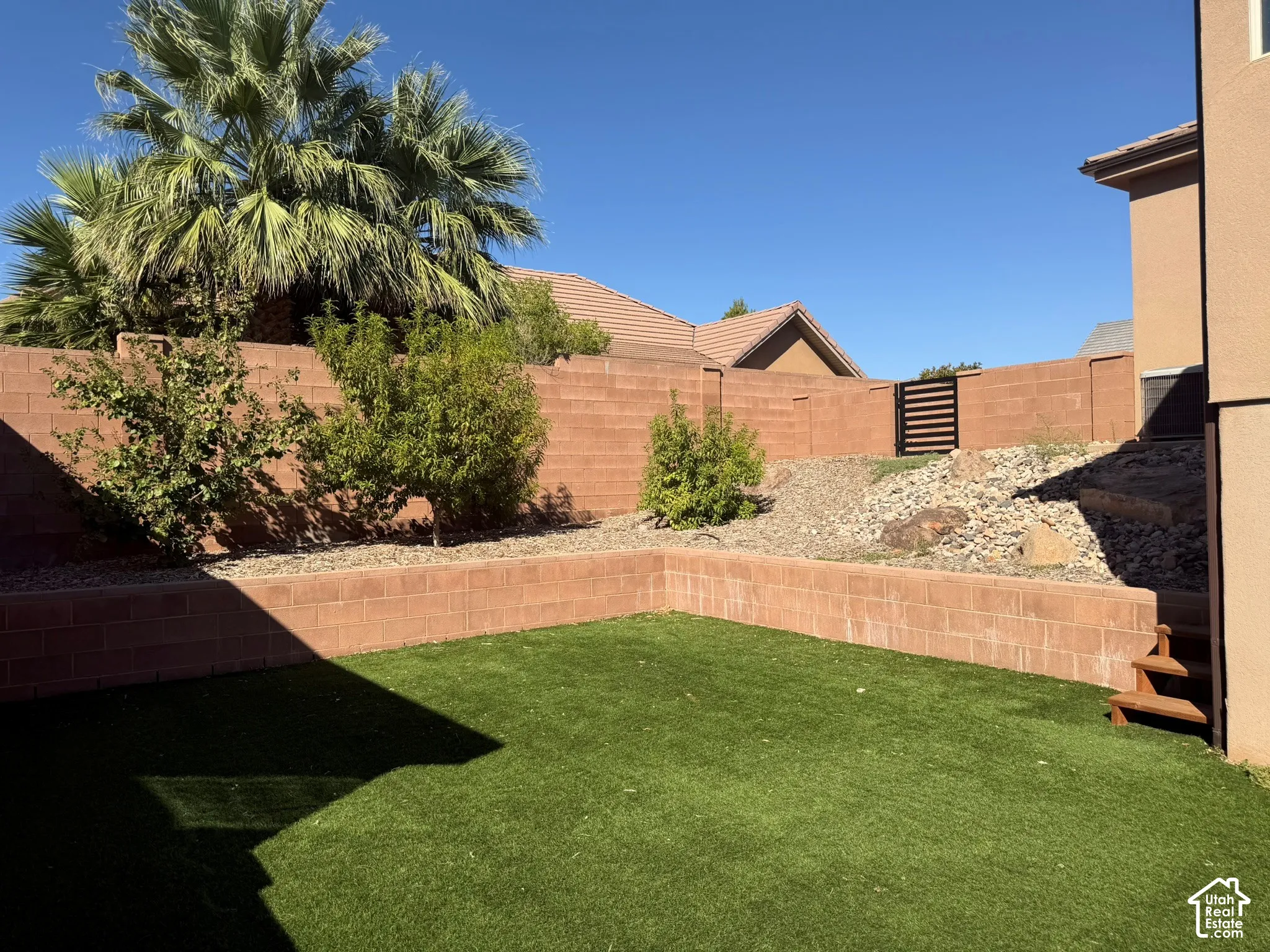 Tiered backyard featuring artificial turf, retaining walls, desert landscaping, and a slatted privacy gate
