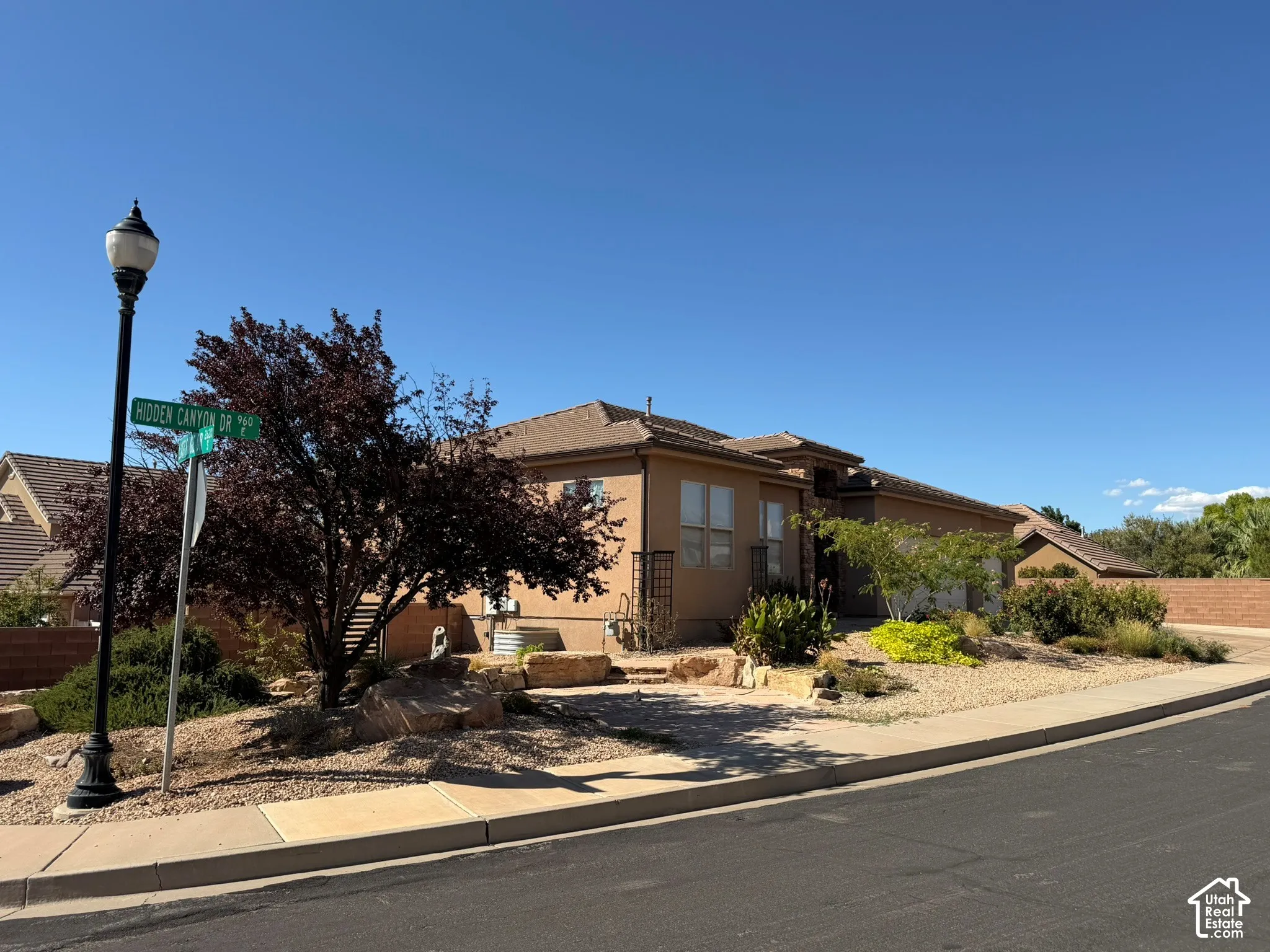 Stucco exterior with a tiled roof, landscaped with mature trees and desert-style plantings, and a concrete sidewalk