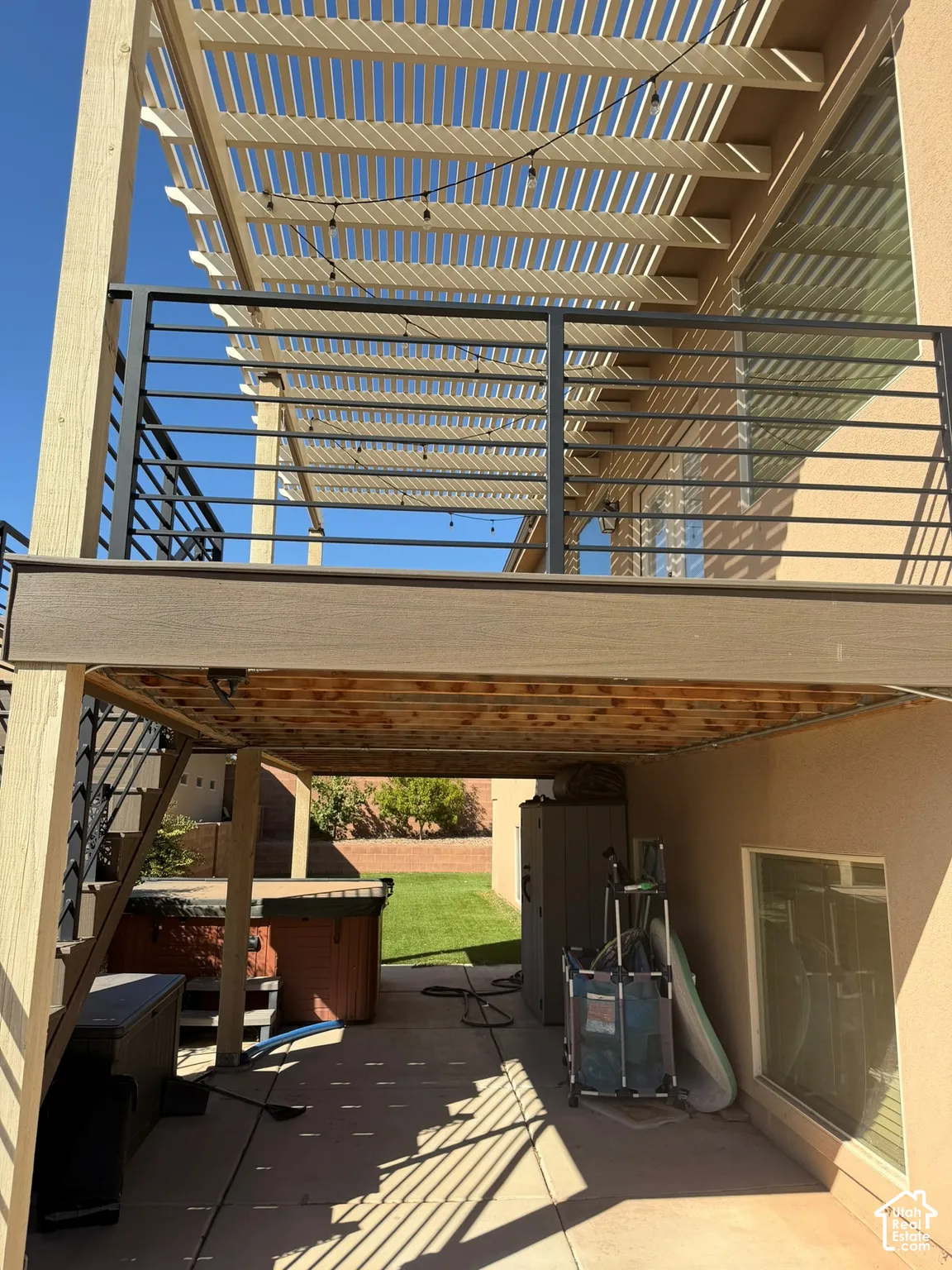 Upper-level deck with a slatted pergola, featuring black metal railings and wood-finish decking