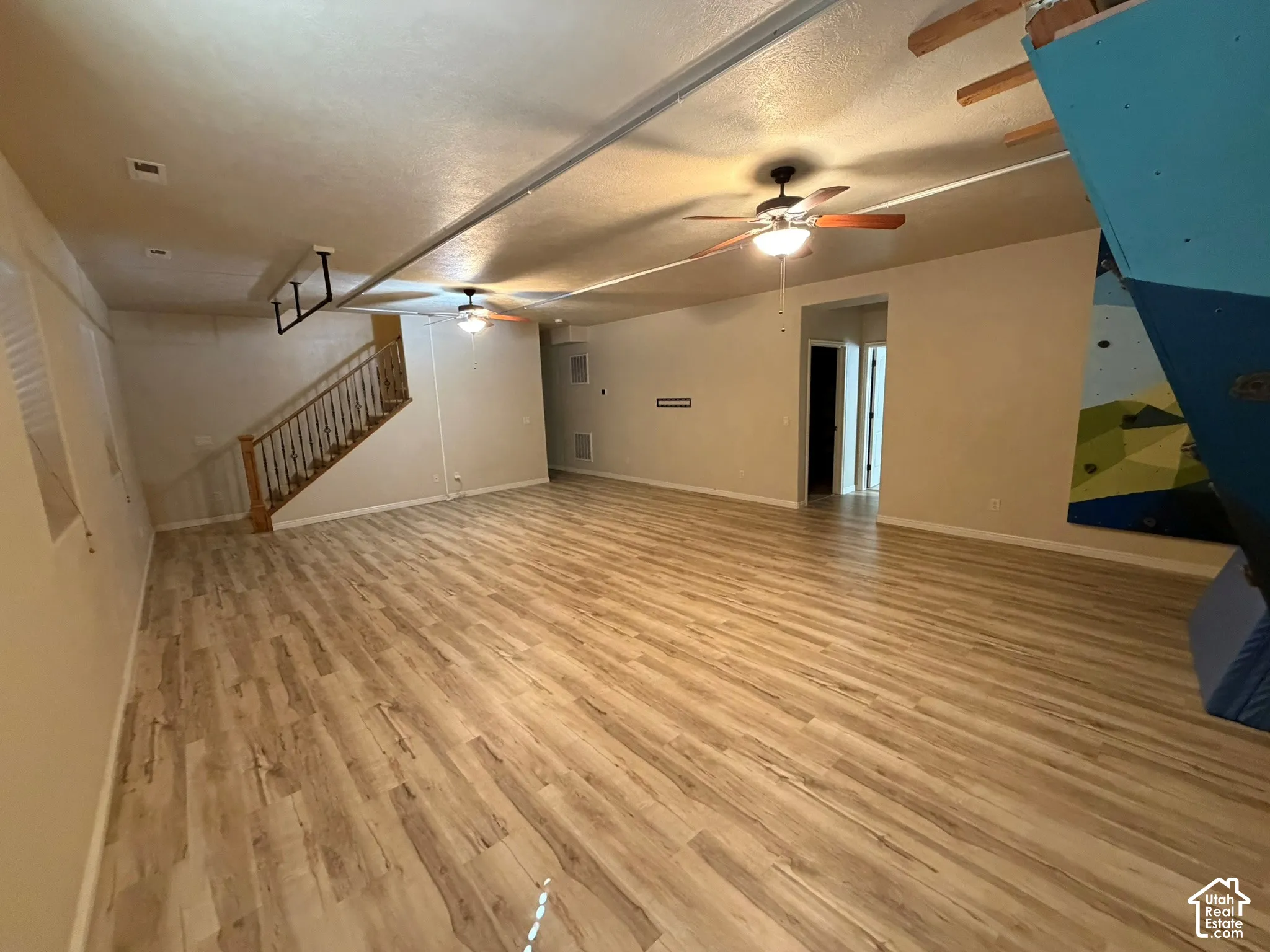 Expansive open-concept room featuring wood-finish flooring, two ceiling fans with integrated lighting, and a prominent staircase with wood railing