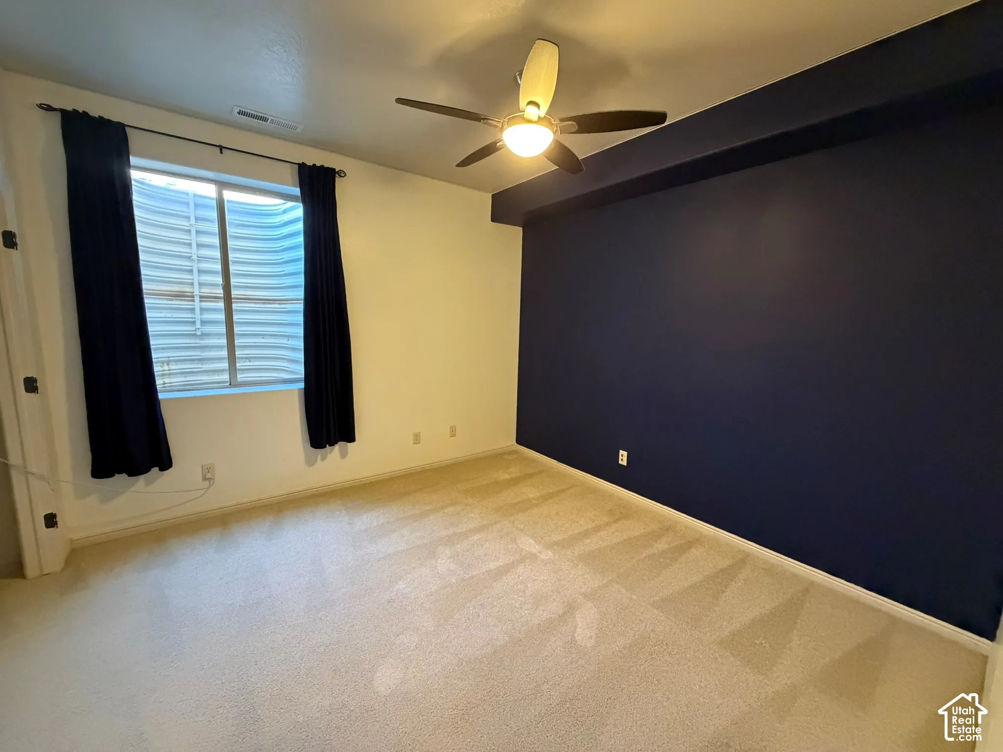 Carpeted room with a ceiling fan, a window, and a dark accent wall