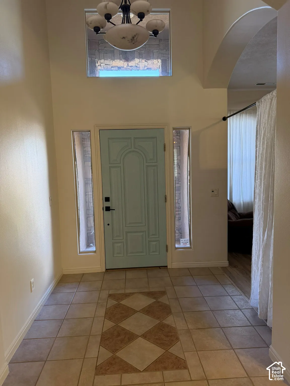 Two-story entryway featuring a decorative light fixture, transom window, and tile flooring with a patterned inlay
