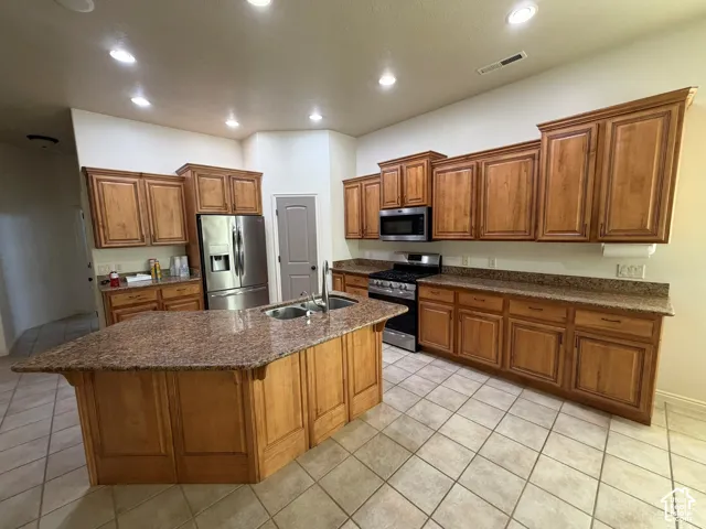 Kitchen featuring an island with a sink, granite countertops, wood cabinetry, and stainless steel appliances