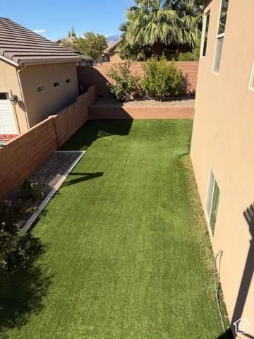 Enclosed yard featuring artificial turf, tiered retaining walls, and established landscaping