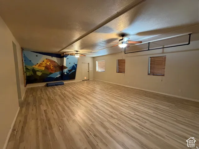 Expansive room featuring wood-finish flooring, two ceiling fans, multiple windows with blinds, and a climbing wall with handholds