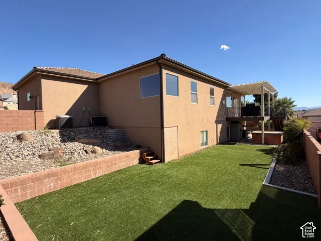 Expansive artificial turf backyard with tiered landscaping, a built-in privacy wall, and a raised composite deck featuring a slatted pergola