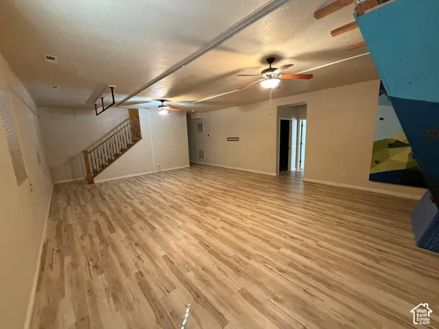 Expansive open-concept room featuring wood-finish flooring, two ceiling fans with integrated lighting, and a prominent staircase with wood railing