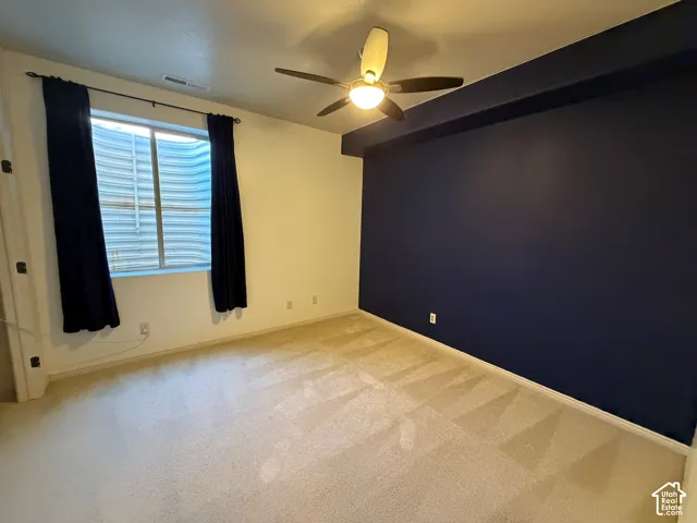 Carpeted room with a ceiling fan, a window, and a dark accent wall